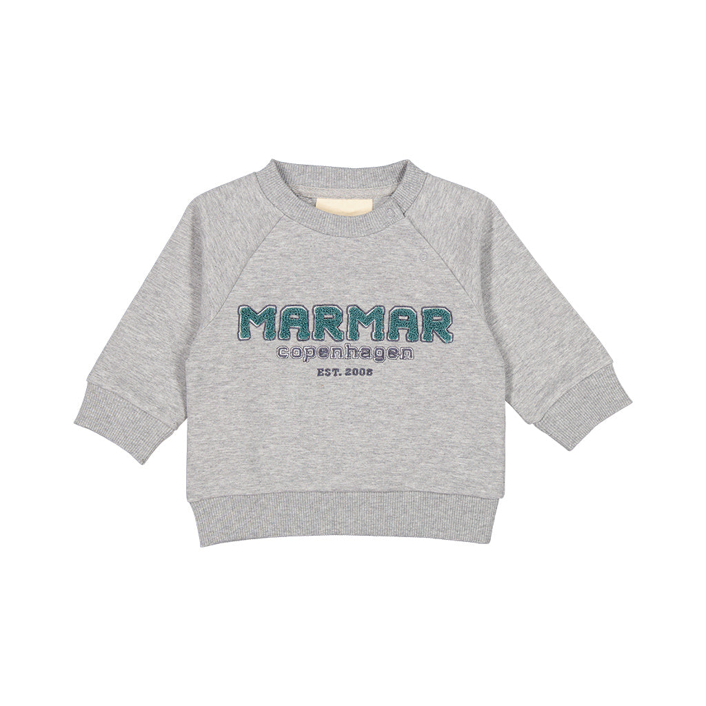Marmar Theos Baby Sweater is een fijne grijze sweat met groen Marmar logo in teddy stof. De grijze sweat heeft een lossere fit en raglan mouwen en boorden in zachte ribkwaliteit aan mouwen, taille en in de hals. Er zitten drukknoopjes bij de linker schouder. 