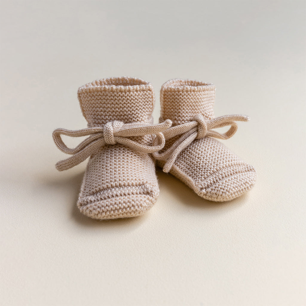 Hvid merinowollen booties in Oat. Beige gebreide babyslofjes die niet afzakken met vetertjes